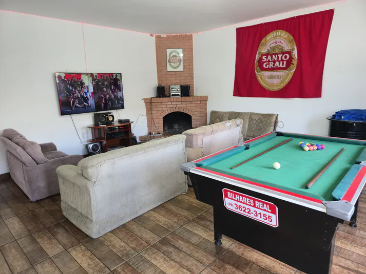 Visão geral da sala de estar da república com TV, pufes confortáveis e iluminação natural