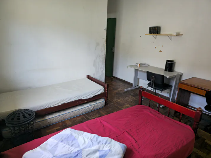 Ângulo alternativo do quarto duplo com suíte, destacando estações de estudo e armários